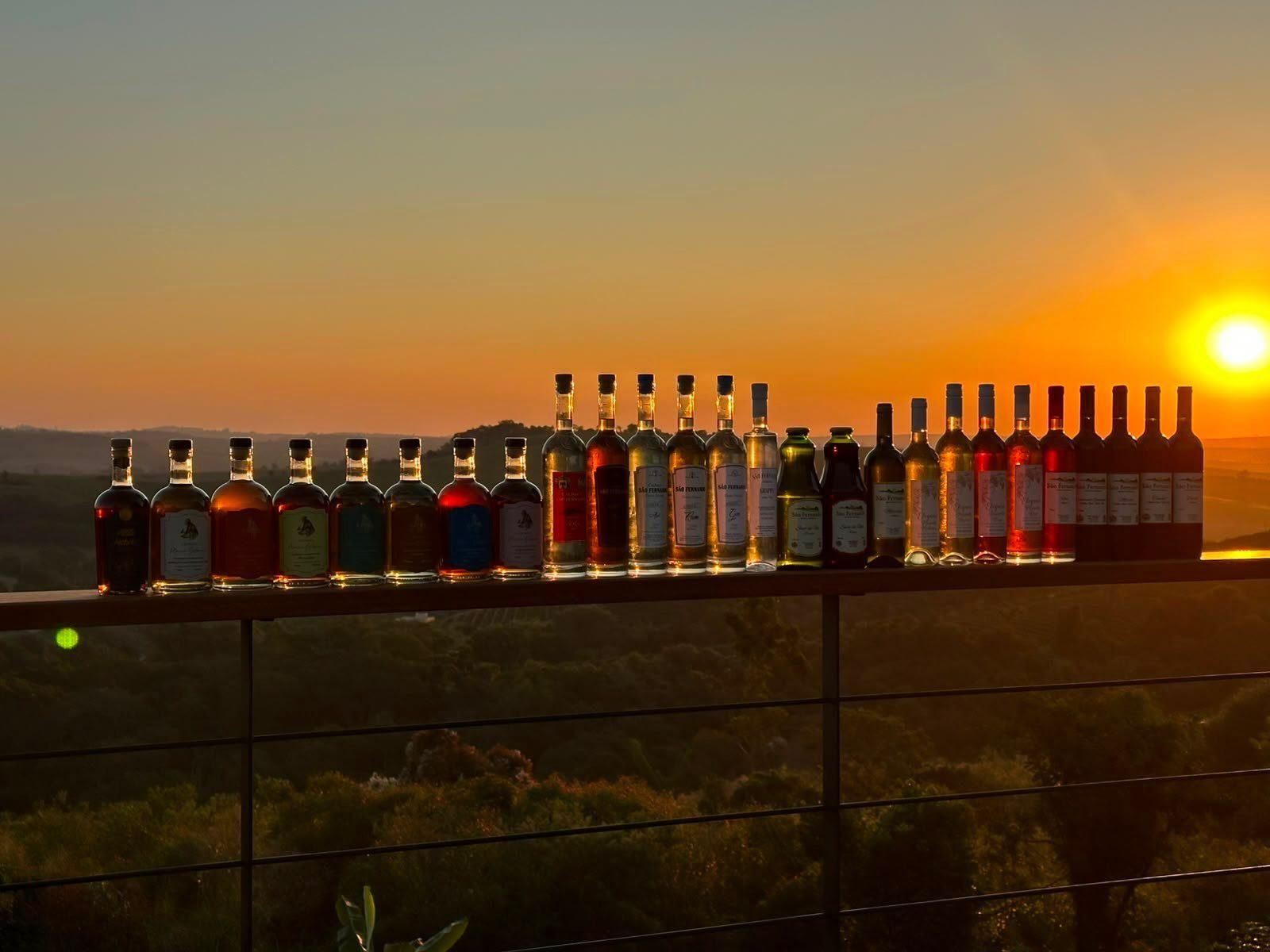 A linha de garrafas do sítio enfileirada no parapeito, com o sol se pondo sobre os morros