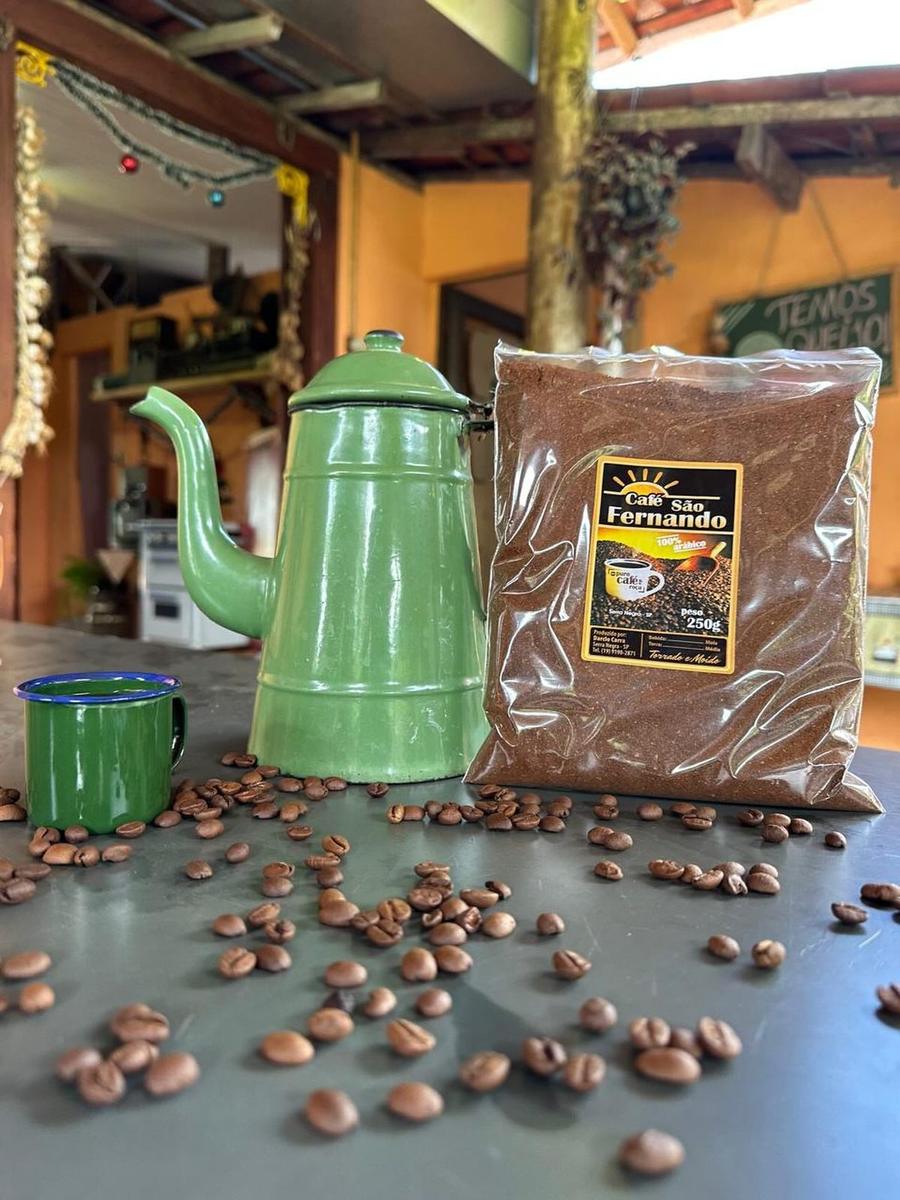 Pacote de Café Premium São Fernando com um bule esmaltado verde e grãos sobre a mesa
