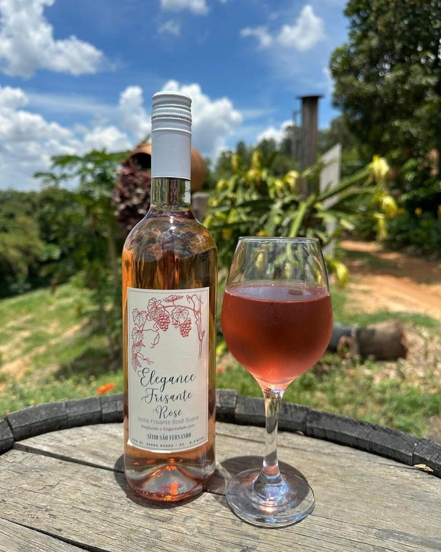 Garrafa e taça de Frisante Moscato Rosé sobre um barril, com o vale ao fundo
