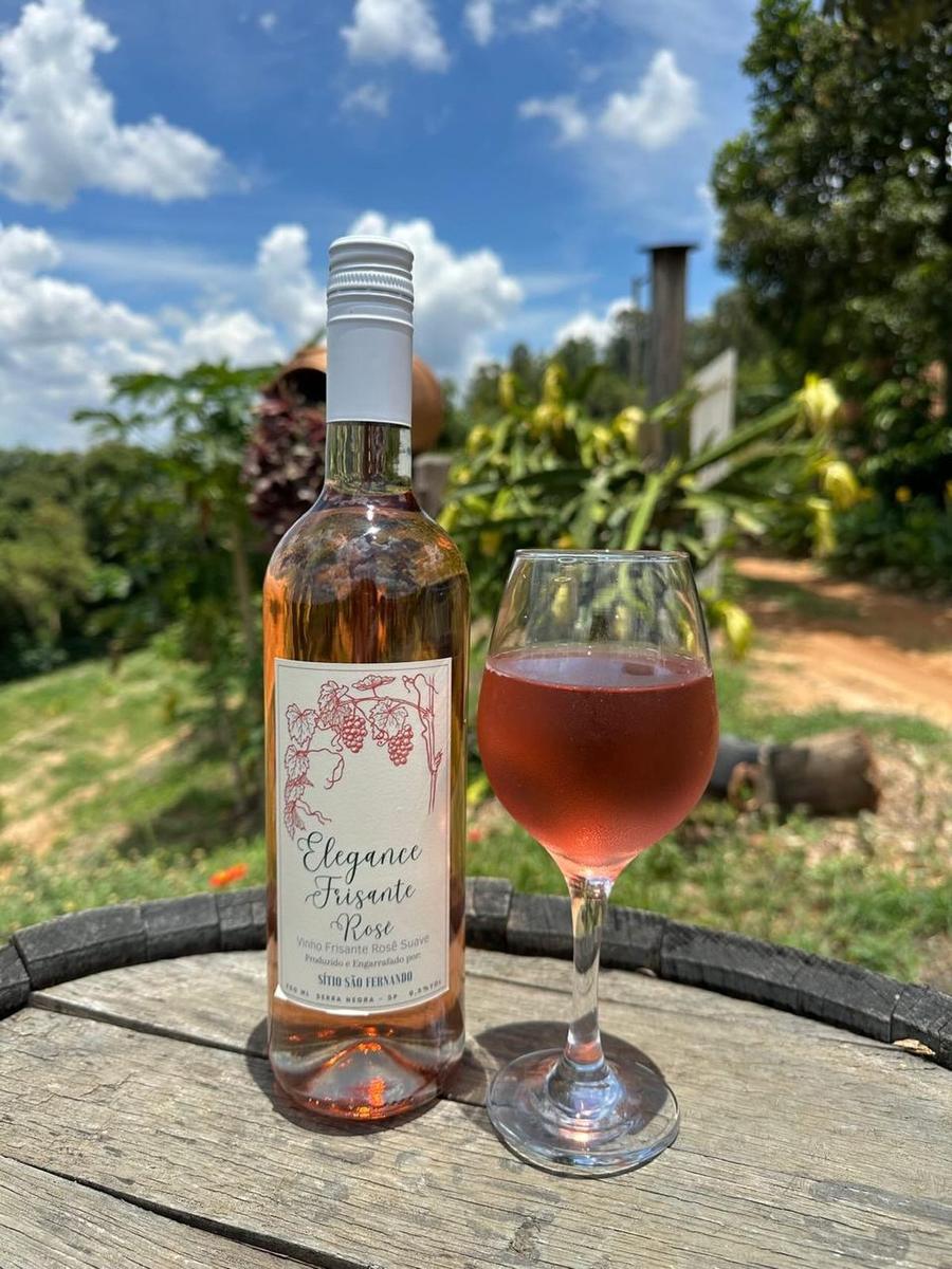 Garrafa e taça de Frisante Moscato Rosé sobre um barril, com o vale ao fundo