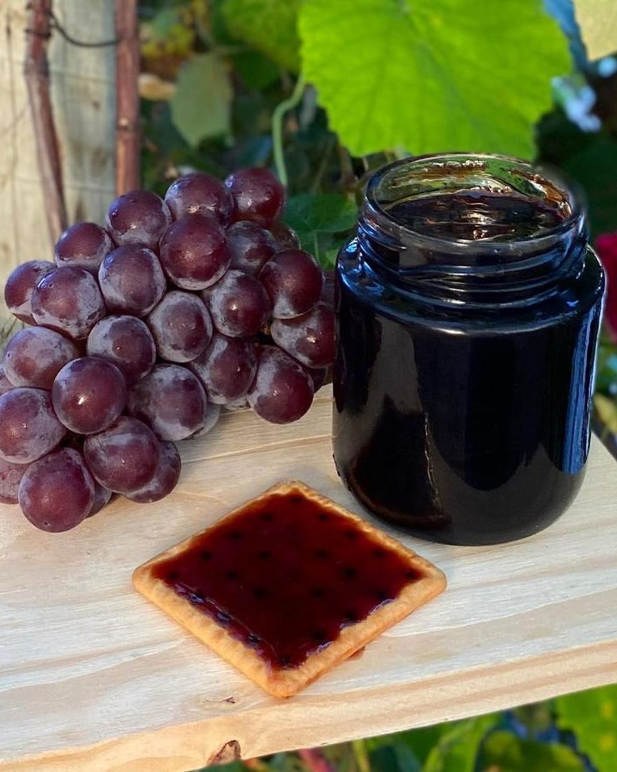 Pote de geleia de uva ao lado de um cacho de uvas e uma torrada