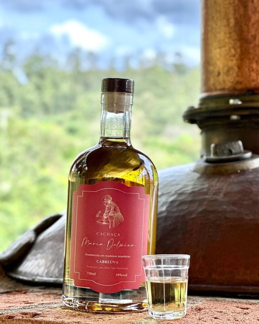 Garrafa da cachaça Maria Delmina Cabreúva diante do alambique de cobre