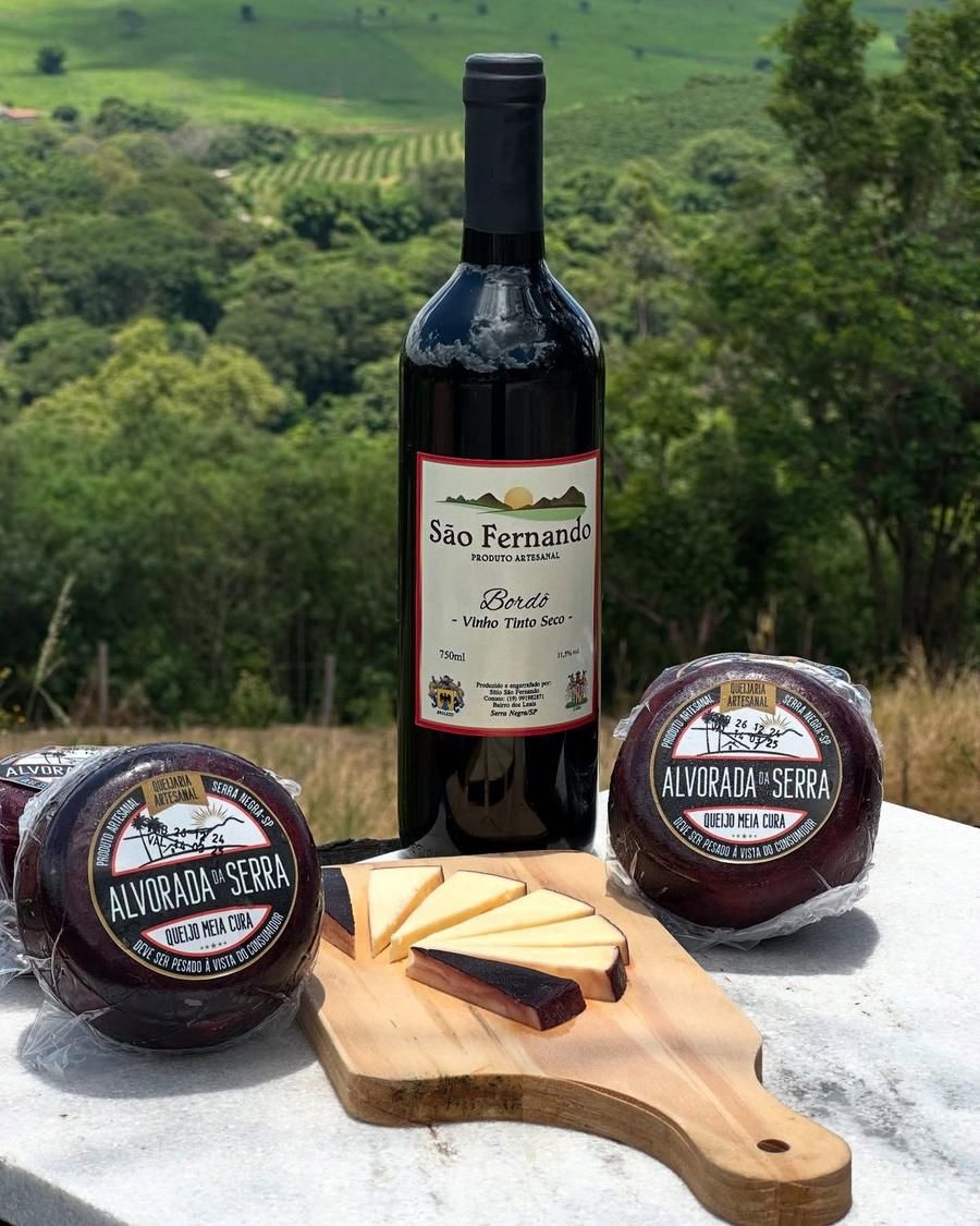 Queijo meia cura fatiado ao lado de uma garrafa de vinho Bordô São Fernando