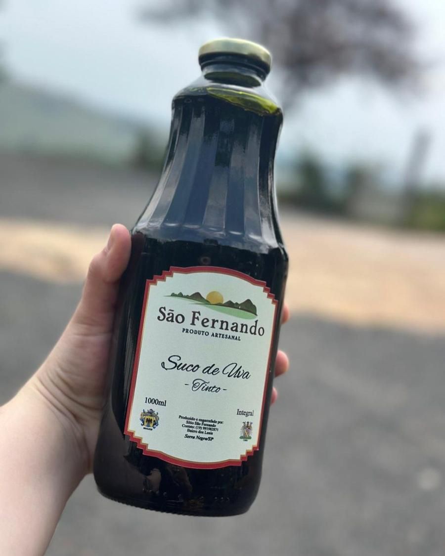 Mão segurando uma garrafa de Suco de Uva Tinto São Fernando