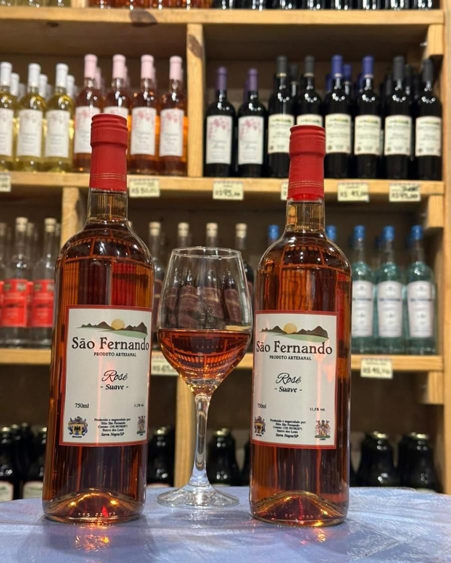Duas garrafas de Rosé Suave e uma taça, diante das prateleiras da loja